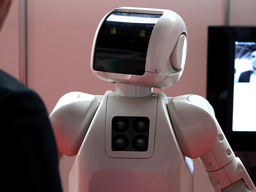 A white robot with a black face plate looks up at a human off-camera.