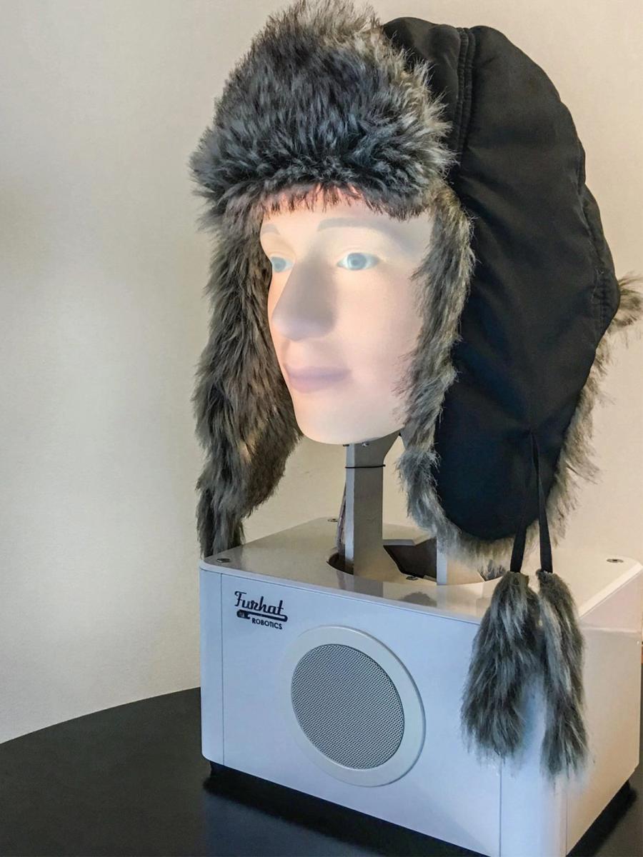 A white base holds a projected robot head that wears a fur hat.