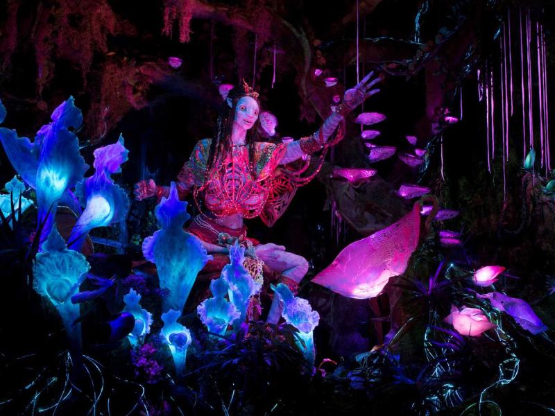 A colorful photo shows a pink and blue lit environment in which a friendly alien-like robot lifts it's arm toward the viewer.