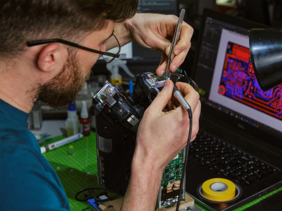A roboticist works with hand tools on the innards of the DEX-EE robotic gripper hand.