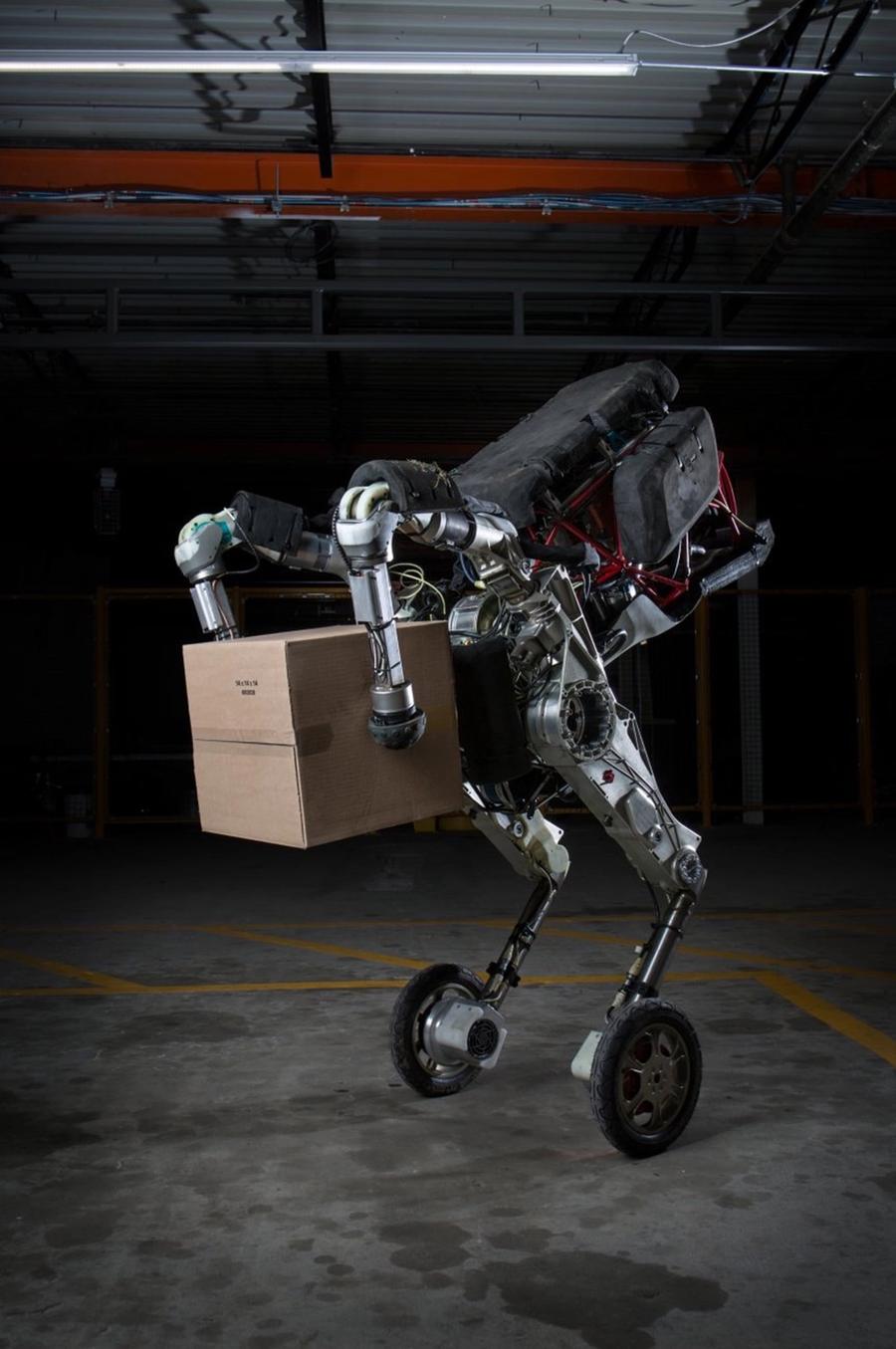 A two wheeled robot balances while holding a package between two balled robotic arms.