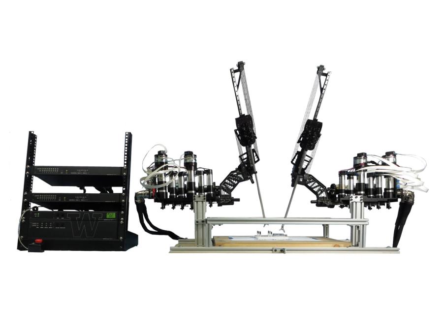 A black multilevel objects sits next to a platform with two black appendages holding surgical tools over an object on the surface.