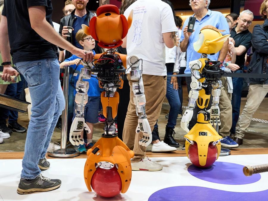 A back view shows two Mirokaï robots at an electronics show.