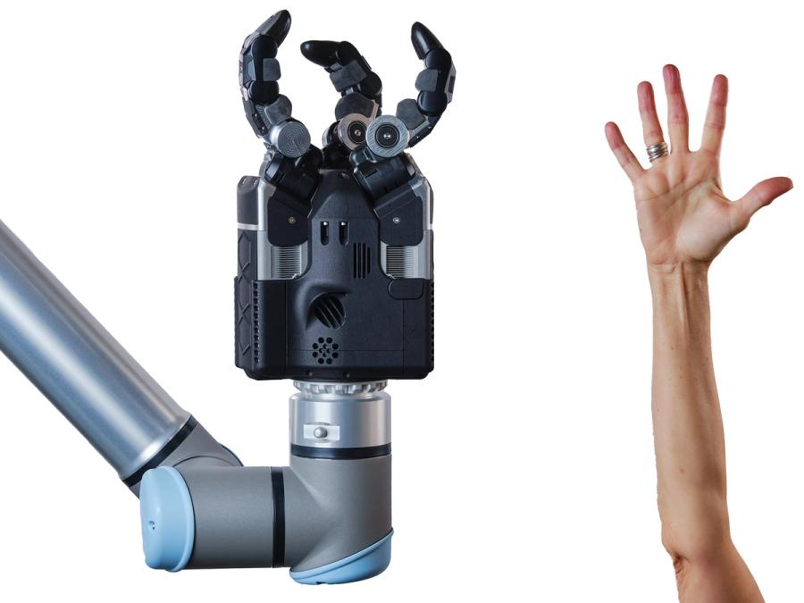 A three fingered black robotic gripper hand on a blue robotic arm compared in size to a human hand and arm. The robot is multiple sizes larger.