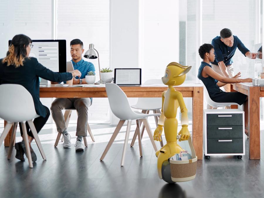 A yellow humanoid robot with a fox-like face wheels in an office carrying a bag of mail.