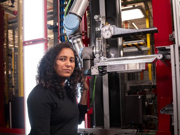 A woman with dark curly hair and a black shirt kneels in front of a robotic system at Amazon.