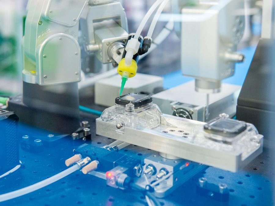 The robot arm has a small yellow and green tool on its end, which it uses to do close and precise work on a black object on a tray.