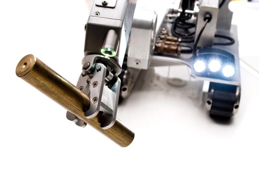 The robots strong metal gripper holds a copper tube.