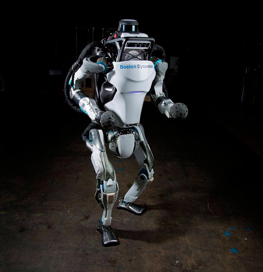 An advanced looking two legged humanoid robot stands on a dark surface.