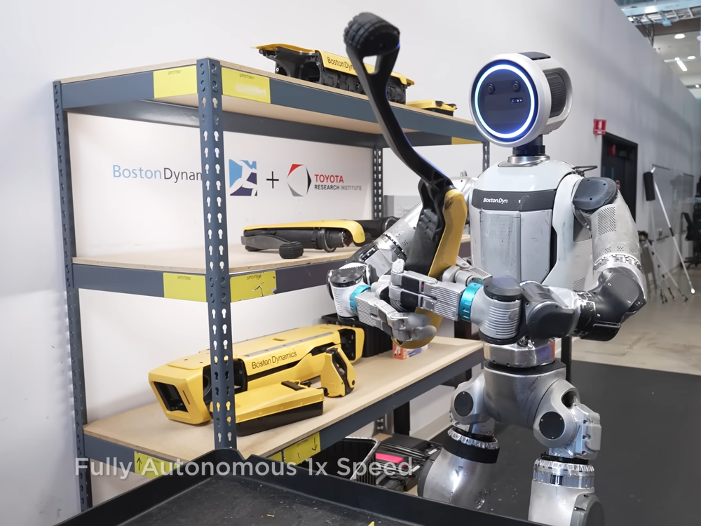 Boston Dynamics robot operating autonomously near stacked robotic components on a shelf.